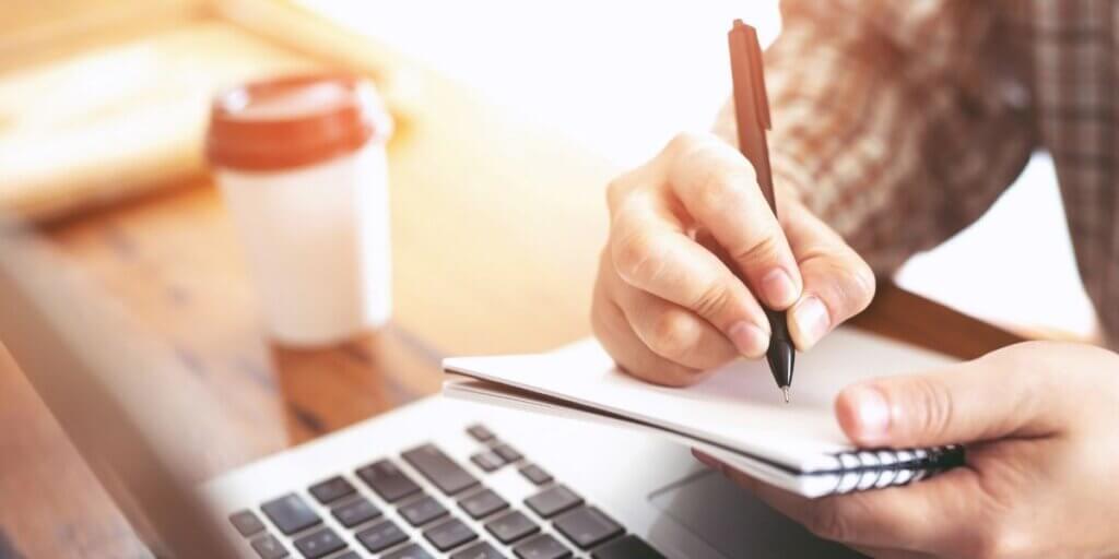Closeup of hands writing on a notepad near laptop